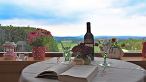 Mesa com livro, garrafa e copos, com vista para uma paisagem deslumbrante.