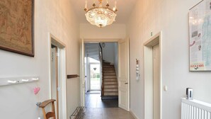 Un couloir doté d’un sol à carreaux, d’un lustre, d’une chaise en bois et d’un escalier menant à une autre pièce.