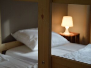En køjeseng med hvidt sengetøj og et natbord med en lampe.
