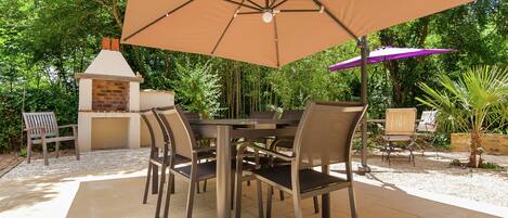 Un patio al aire libre con chimenea de ladrillo, una mesa con sillas y sombrillas que dan sombra.