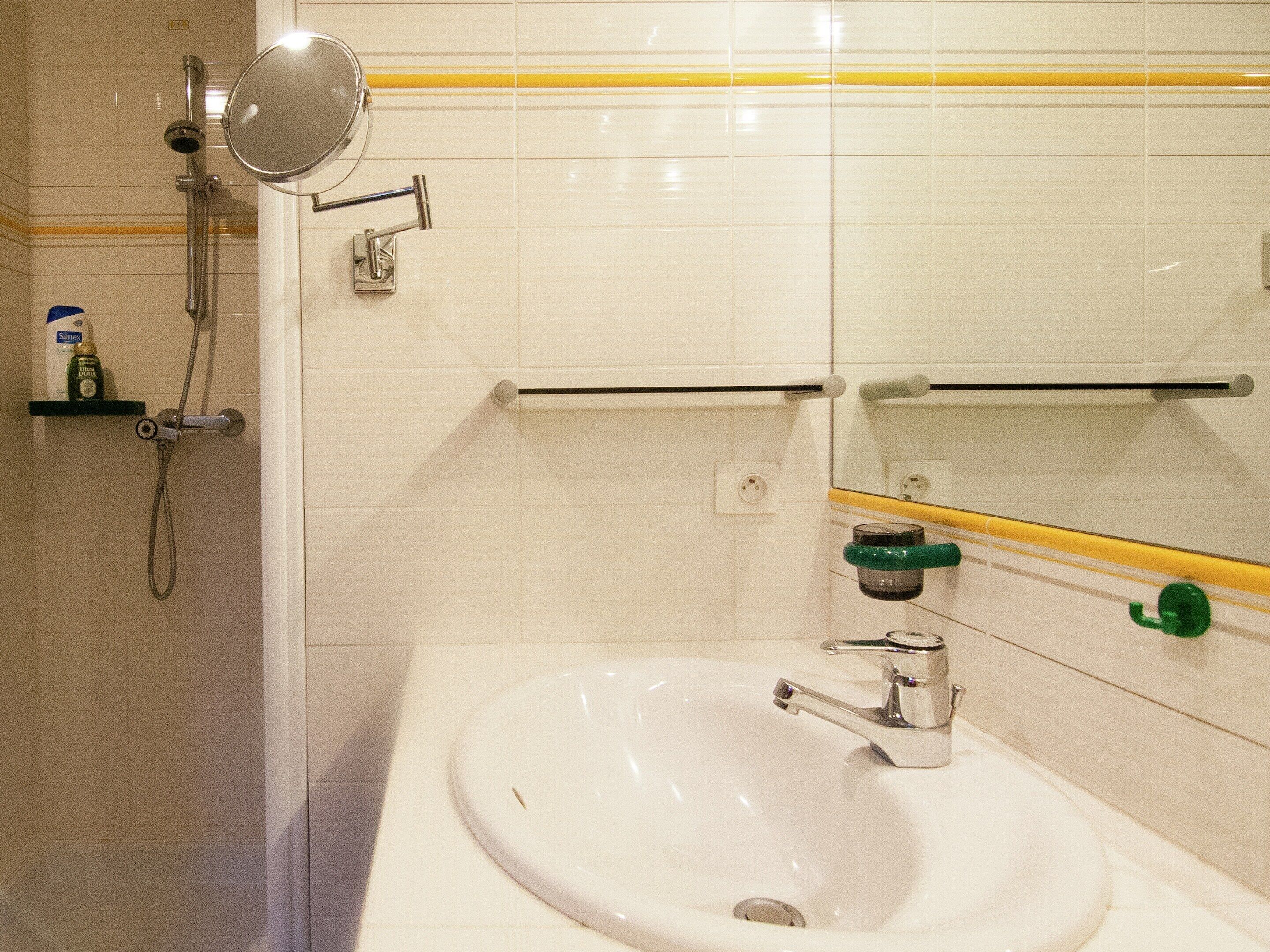 Un baño con lavamanos blanco, espejo de mano, cabezal de ducha y toallero.