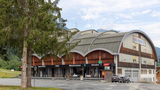A building with a curved roof, labeled 'Millennium-Express,' featuring ticket counters, a depot, and an information desk. - Apartment in Tropolach Near Nassfeld (Hermagor-Pressegger See)
