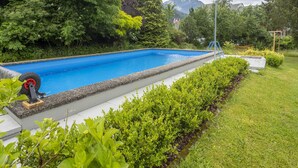 A swimming pool with a paved deck, surrounded by well-maintained greenery and a mountain in the background. - Apartment in Tropolach Near Nassfeld (Hermagor-Pressegger See)