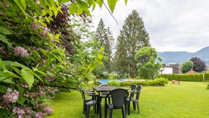 A grassy outdoor area with a table and chairs, a swimming pool, and trees in the background. - Apartment in Tropolach Near Nassfeld (Hermagor-Pressegger See)