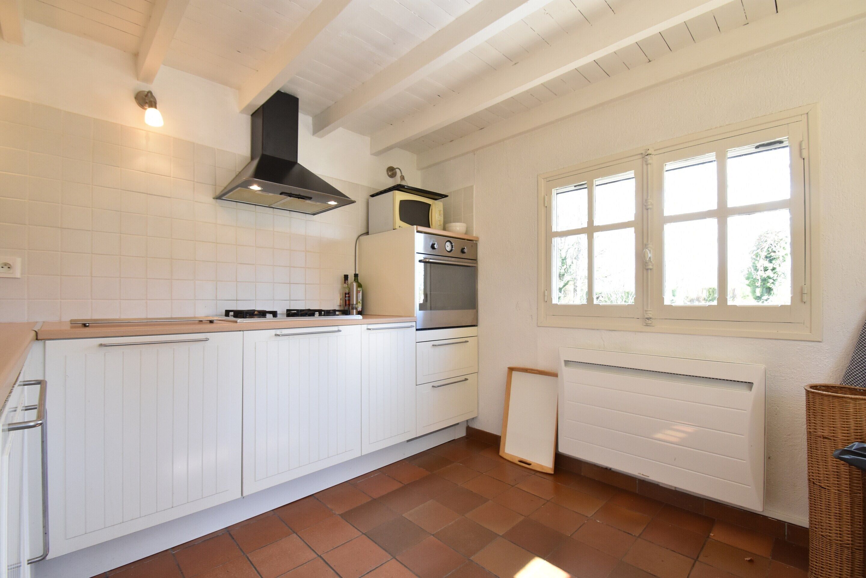 Une cuisine avec des meubles blancs, une cuisinière, un four à micro-ondes et une fenêtre avec des stores.