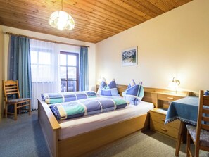 A bedroom with a wooden bed, a desk, a chair, and a window with curtains.