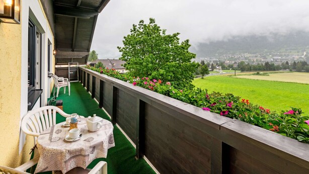 A balcony with a table set for tea, overlooking a green field and a town in the distance.
