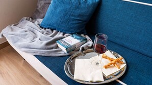 A cozy seating area with a blue sofa, a blanket, a book, a glass of red wine, and a tray with food and napkins.