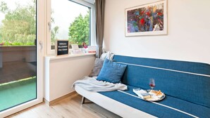 A modern room with a blue sofa, a glass door leading to a balcony, a framed abstract painting, and a welcome sign.