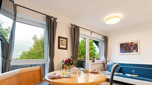 A cozy room with a wooden table, chairs, a sofa, and a large window offering a view of greenery.