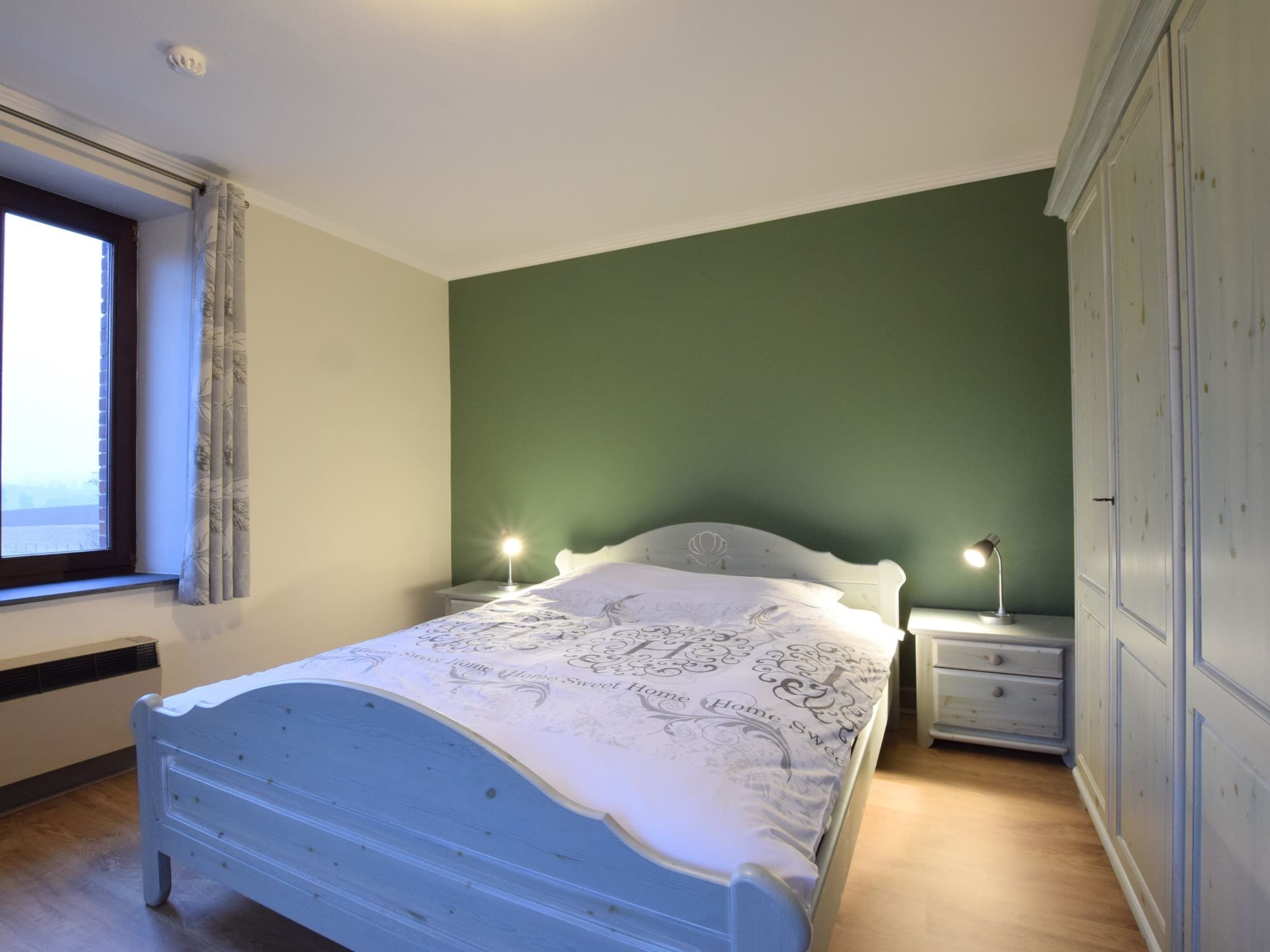 A bedroom with a bed, two bedside tables, a window with curtains, and a wardrobe.