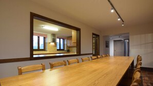 A conference room with a long wooden table, chairs, a large mirror, and a view of the kitchen through the mirror. - Holiday Home in Rogery With Sauna (Gouvy)