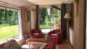 A room with a large sliding glass door, two red leather chairs, a wooden coffee table, and a sofa. - Cottage Near the Mill Pond With a Beautiful Garden (Vitz-sur-Authie)