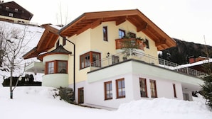 A two-story house with a sloped roof, wooden beams, and a balcony with a potted plant. - Sunlit Apartment near Ski Area in Hüttschlag (Huettschlag)