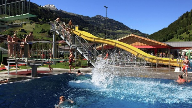 A swimming pool with a water slide, surrounded by a mountainous landscape. - Sunlit Apartment near Ski Area in Hüttschlag (Huettschlag)