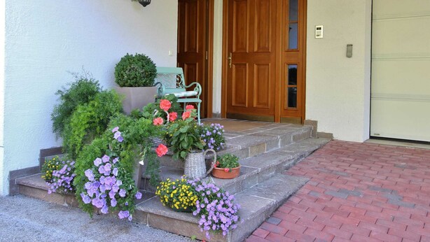 Une entrée avec une porte en bois, un banc et un jardinier orné de fleurs.