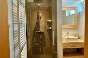 Un baño moderno con ducha envuelta en cristal, tocador de madera y espejo sobre el lavamanos.