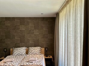 A bedroom with a bed, two bedside tables, a lamp, and a curtain.