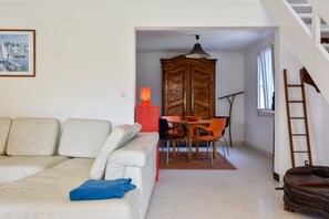 Ein Wohnzimmer mit einem weißen Sofa, einem Esstisch mit Stühlen, einer Holzkommode und einer Treppe.