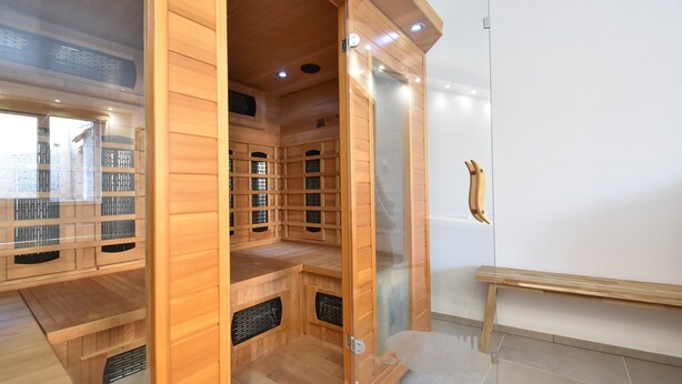 Uma sala de sauna com bancos de madeira, porta de vidro e um banco do lado de fora.
