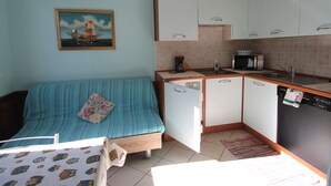 A compact room with a bed, a kitchenette, and a painting on the wall. - Apartment 2 in Baita Near the Ski Lifts (Livigno)