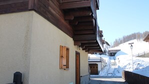 A snow-covered street with wooden buildings, a wooden fence, and a snow-covered slope in the background. - Apartment 2 in Baita Near the Ski Lifts (Livigno)