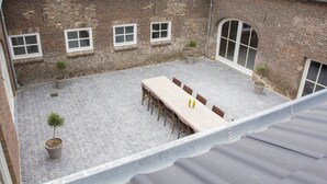 A courtyard with a long table and chairs, potted plants, and a brick building with windows. - Holiday Home With Sauna (Swolgen)