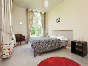 Un dormitorio con una cama, una silla, una mesita de noche, una ventana con cortinas y una alfombra roja.