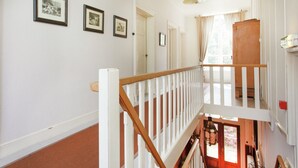 Un escalier avec des rampes blanches et une main courante en bois, menant à un niveau inférieur. Des tableaux encadrés sont accrochés au mur au-dessus de l’escalier.