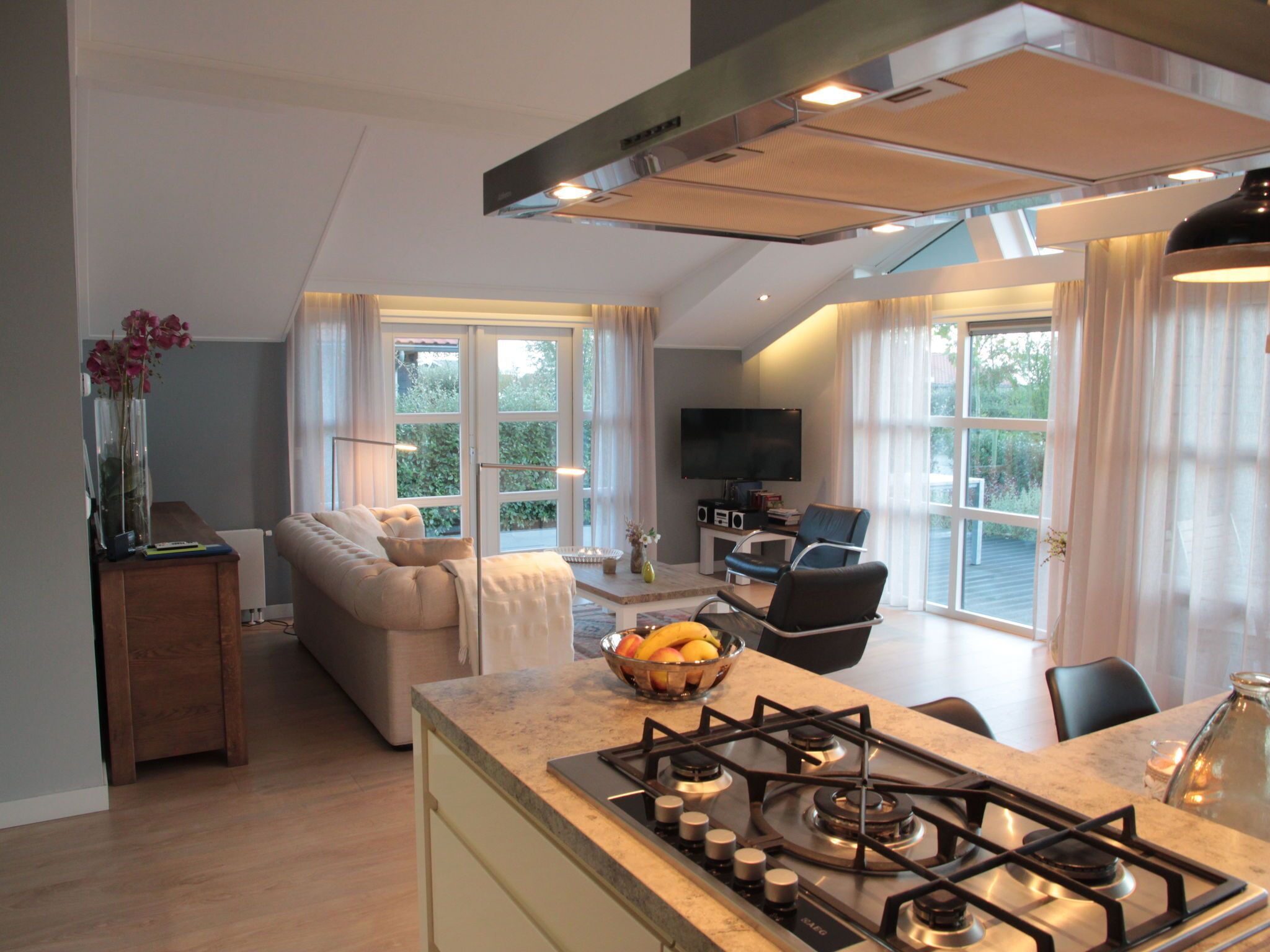 A modern kitchen with a gas stove, a dining area with a table and chairs, a sofa, and a TV in a living room.