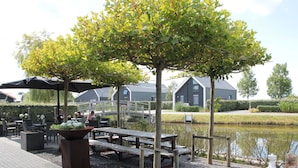 An outdoor patio area with tables and chairs, a bicycle, and a pond. - Comfortable and Tasteful Holiday Home Near the Oosterschelde (Kattendijke)