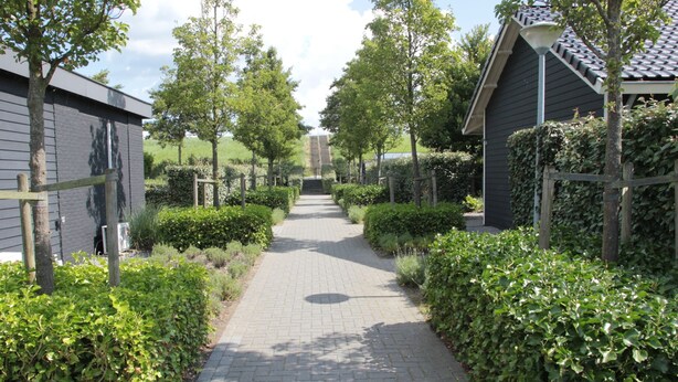 A paved pathway flanked by neatly trimmed hedges and trees, leading towards a building with a dark facade. - Comfortable and Tasteful Holiday Home Near the Oosterschelde (Kattendijke)