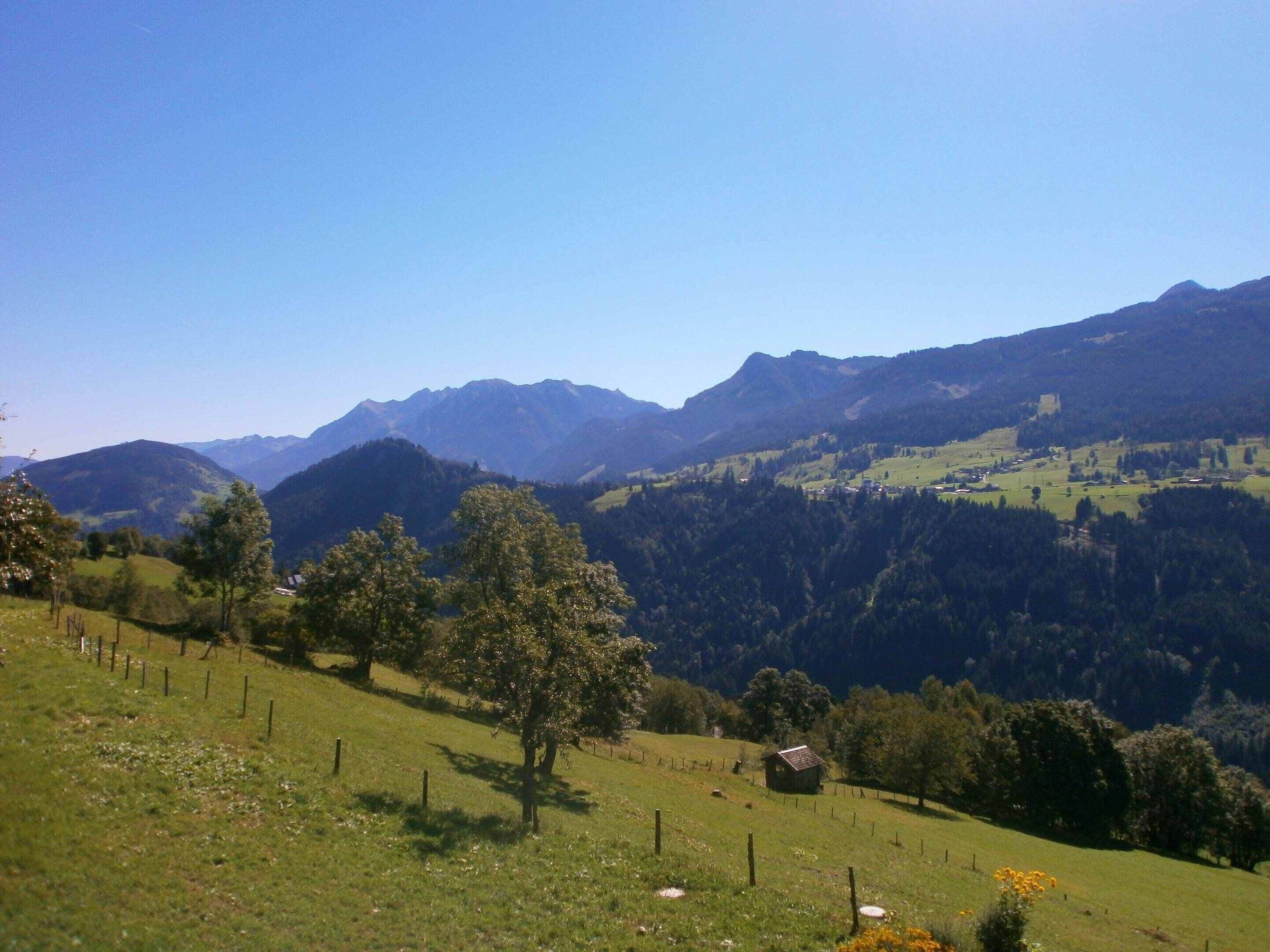 A rural landscape with rolling hills, a small wooden cabin, and a clear blue sky.