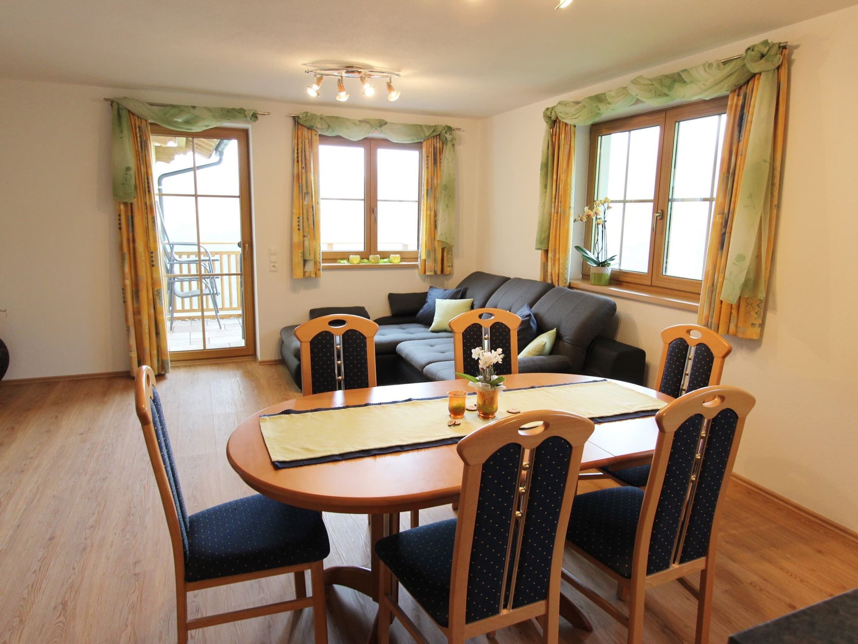 A dining area with a round wooden table, four chairs, and a sofa in the background.
