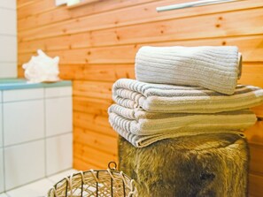 A stack of towels on a wooden stool in a room with wooden walls and a tiled floor.