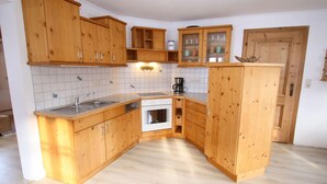 Eine kleine Küche mit Holzschränken, einem Geschirrspüler, einem Backofen und einer Kaffeemaschine.