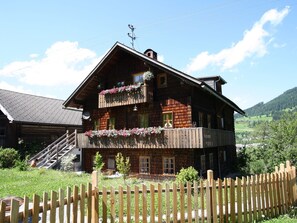 A wooden chalet with a balcony, a staircase, and a wooden fence in the foreground.