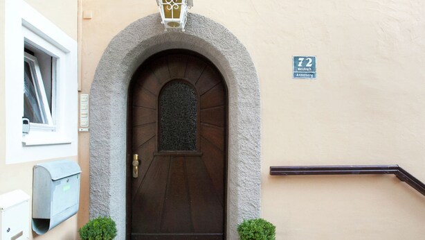 Una puerta marrón con un arco de piedra, un ventanal pequeño y una placa con el número de la dirección.