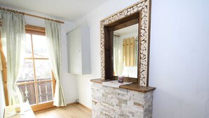 Una habitación con chimenea de piedra, piso de madera, ventana con cortinas y un mueble de madera.