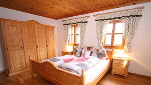 Una cama con estructura de madera, colcha, dos mesitas de noche con lámparas y un armario de madera.