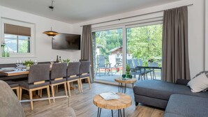 A modern living room with a dining area, a sofa, and a TV mounted on the wall. - Chalet in Muhlbach Near Ski Amade (Muehlbach Am Hochkoenig)