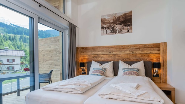 A double bed with a wooden headboard, two bedside tables with lamps, and a large window with a view of a mountain and forest. - Chalet in Muhlbach Near Ski Amade (Muehlbach Am Hochkoenig)
