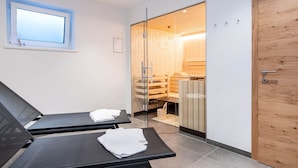 A modern spa room with two reclining chairs, a wooden door, and a glass partition leading to a sauna area. - Chalet in Muhlbach Near Ski Amade (Muehlbach Am Hochkoenig)