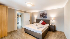 A bedroom with a bed, bedside lamps, a wooden wardrobe, and a door leading to another room.