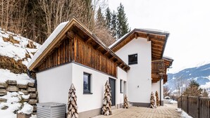 A modern chalet with a wooden facade, a brick entrance, and a snow-covered landscape.