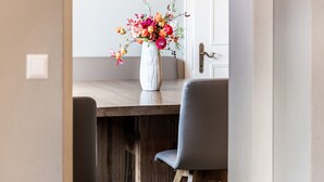 A dining table with a white vase of colorful flowers, two grey chairs, and a wooden floor.