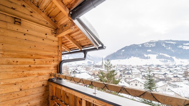 A wooden balcony with a view of a snowy town and mountains.