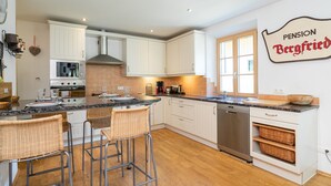 A modern kitchen with white cabinets, a stainless steel range hood, a built-in oven, a dishwasher, and a large island with bar stools. - Spacious Villa in Zell am See near Ski Area (Zell am See)