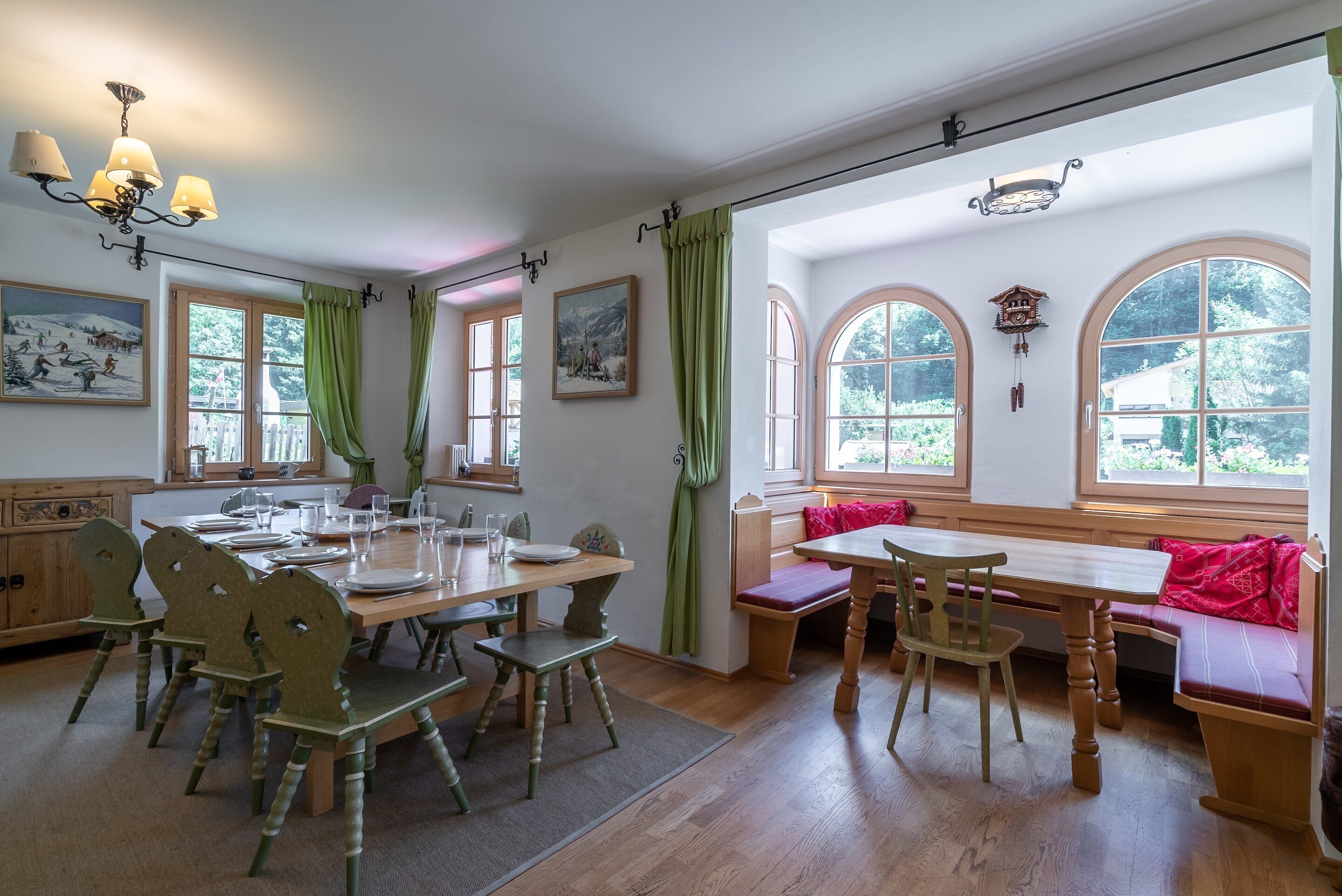 A dining area with wooden tables and chairs, large arched windows, and a chandelier.