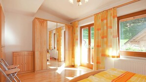 A bedroom with a bed, a chair, a wardrobe, and a window with curtains. - Appartment Roswitha (Wagrain)